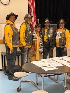 Five people, including a woman in a yellow outfit, stand near a table with papers, men in yellow shirts and vests.