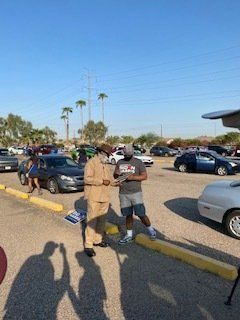 Two men talking in a parking lot filled with cars on a sunny day.