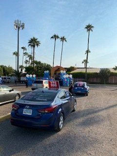 Cars parked near palm trees and portable toilets under a cloudy sky.