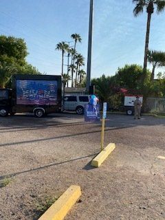 Truck with LED screen parked near a parking meter in an outdoor area with palm trees.