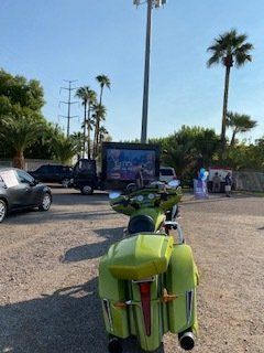 Lime-green three-wheeled motorcycle parked facing away from outdoor movie screen with palm trees in the background.