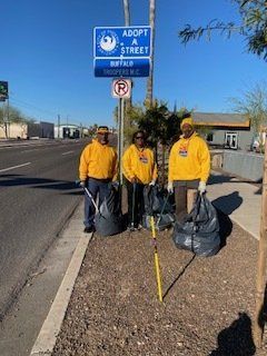 Three people in yellow shirts pick up trash along a road next to an 