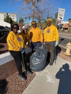 Four people in yellow sweatshirts hold trash pickers and a bag on a sidewalk.