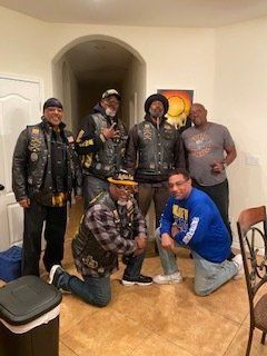 Group of men wearing leather vests, some kneeling, in a home.