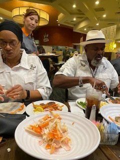 People eating at a restaurant; seafood and sides on the table. A server in background.