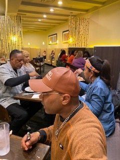 People seated at tables inside a restaurant, eating and interacting. Warm lighting and decor.
