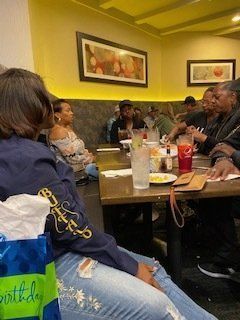 People gathered around a table in a restaurant. One person has a birthday gift. Yellow walls, dim lighting.