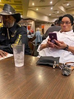 Person wearing cowboy hat and person on phone sitting at a table in restaurant.