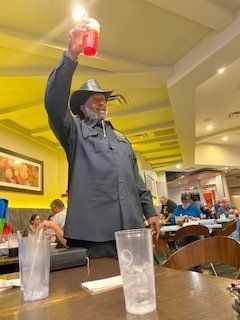 Man in cowboy hat raises a pink drink in a restaurant, toasting.