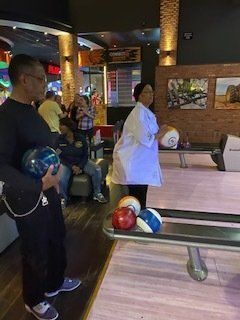 People bowling indoors. One holds a ball, another prepares to throw. Bowling balls in foreground.