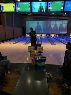 Person bowling at an alley, large screen behind showing a movie.