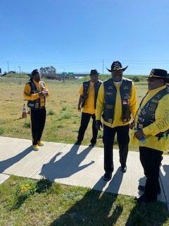 Four people in yellow shirts, black vests, and hats stand outdoors on a sunny day.