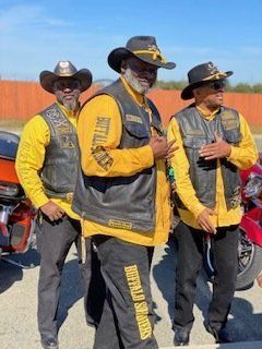 Three people in black vests, yellow shirts, and cowboy hats; posing outside near motorcycles.