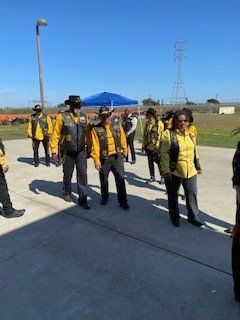 Group of people in yellow shirts, black vests, and hats walking outside on a sunny day.