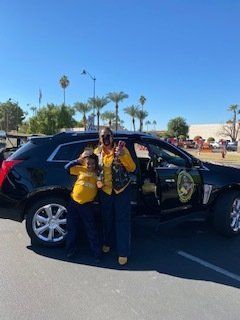 A person and a child in yellow tops stand by a black SUV in a sunny outdoor setting.
