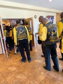 Group of people wearing yellow and black vests, entering a building. The vests read “Buffalo Soldiers”.