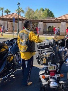 Man in biker vest standing near motorcycles, outdoors, sunny day.