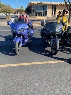 Two motorcycles parked on pavement, one blue, one black. Rider in yellow jacket on black bike.