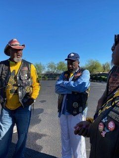 Three men wearing vests, gathered outdoors; blue sky backdrop.