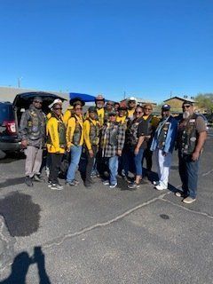 A group of people wearing jackets with patches, standing in a parking lot on a sunny day.
