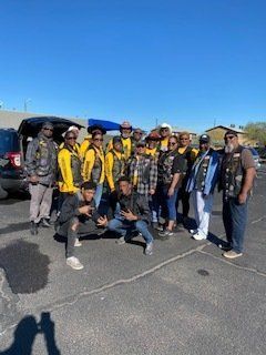 Group of people, many in yellow vests, pose outdoors. Some are squatting, smiling, and flashing hand signs.
