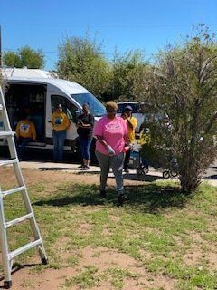 People standing by a van and a bush on a sunny day. A ladder is in the foreground.