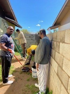 People painting a concrete block wall outdoors on a sunny day.