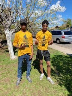 Two people in yellow shirts, black caps, and jeans/shorts, posing outdoors.