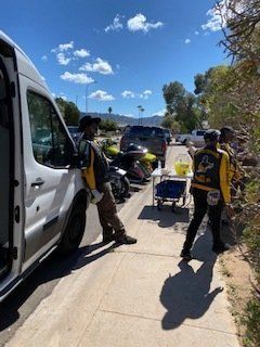 People by a white van and service cart on a sunny day.