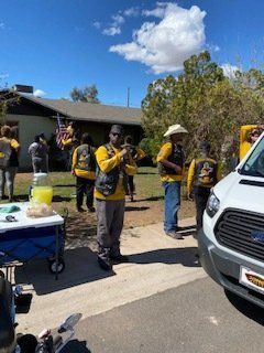 Group of people in yellow shirts, standing in front of a house, some near a white van.