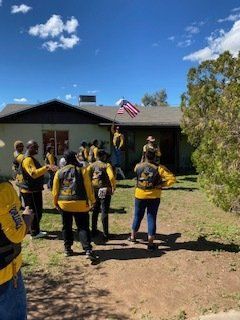 Group in yellow vests outside a house; one holds an American flag aloft.