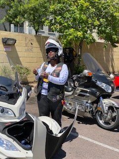 Person wearing a helmet stands near motorcycles, with open side luggage. Sunny, outdoor setting.