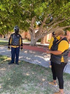 Two people stand outside, one in a helmet and vest, other in a mask and vest.
