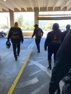 Motorcyclists walking in a parking garage. They wear black jackets with patches.