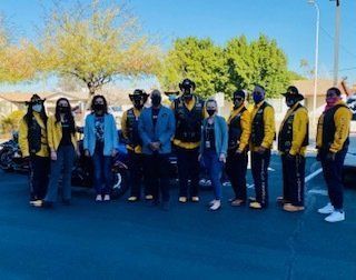 Group of people, some wearing yellow vests, standing by a motorcycle outdoors, possibly at an event.