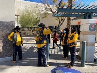 Group of people in yellow vests and masks standing outdoors near a building.