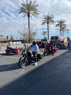 Motorcyclists on Harley-Davidsons parked outdoors under palm trees on a sunny day.