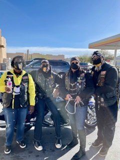 Group of bikers posed in front of a gas station, wearing vests, bandanas, and sunglasses.
