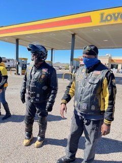 Two people in biker jackets and helmets stand in front of a Love's gas station.