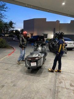 Two people with helmets and jackets near a motorcycle, possibly outdoors at dusk.