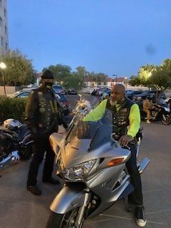 Two men in biker vests with motorcycles parked outside at dusk.