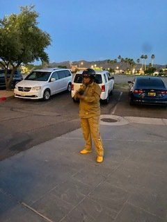 Person in tan outfit standing in a parking lot, holding an object, near parked cars.