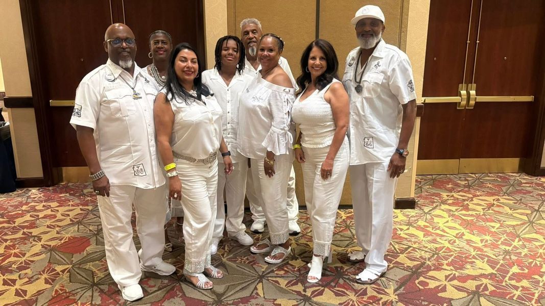 Group of people in white outfits pose together indoors.