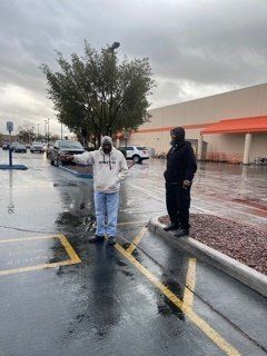 Two people standing in a wet parking lot, near a building. One points. Overcast sky.