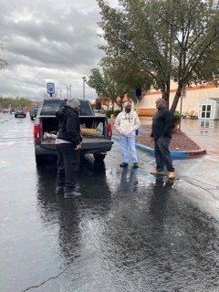 Three people standing near a truck in a wet parking lot. Cloudy sky, reflecting on the pavement.