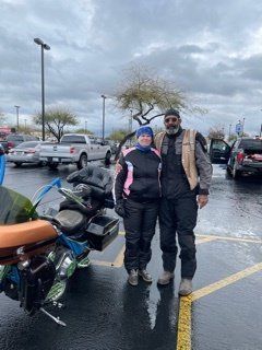 Two people standing in a parking lot next to a motorcycle on a cloudy day.