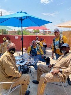 Group of people in yellow shirts and tan outfits at an outdoor patio with umbrellas, smiling.