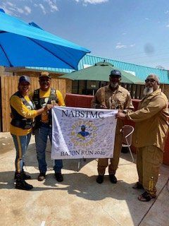 Group holding a signed flag outdoors; blue umbrella, sunny day.