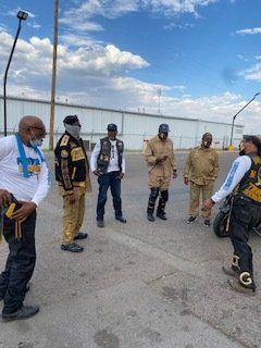 Group of people in vests standing outside, near a motorcycle and a warehouse.