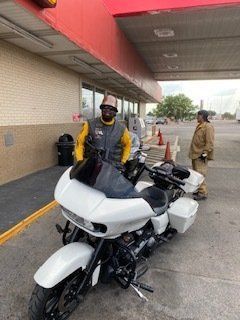 Person standing next to a white motorcycle at a gas station, another person nearby.